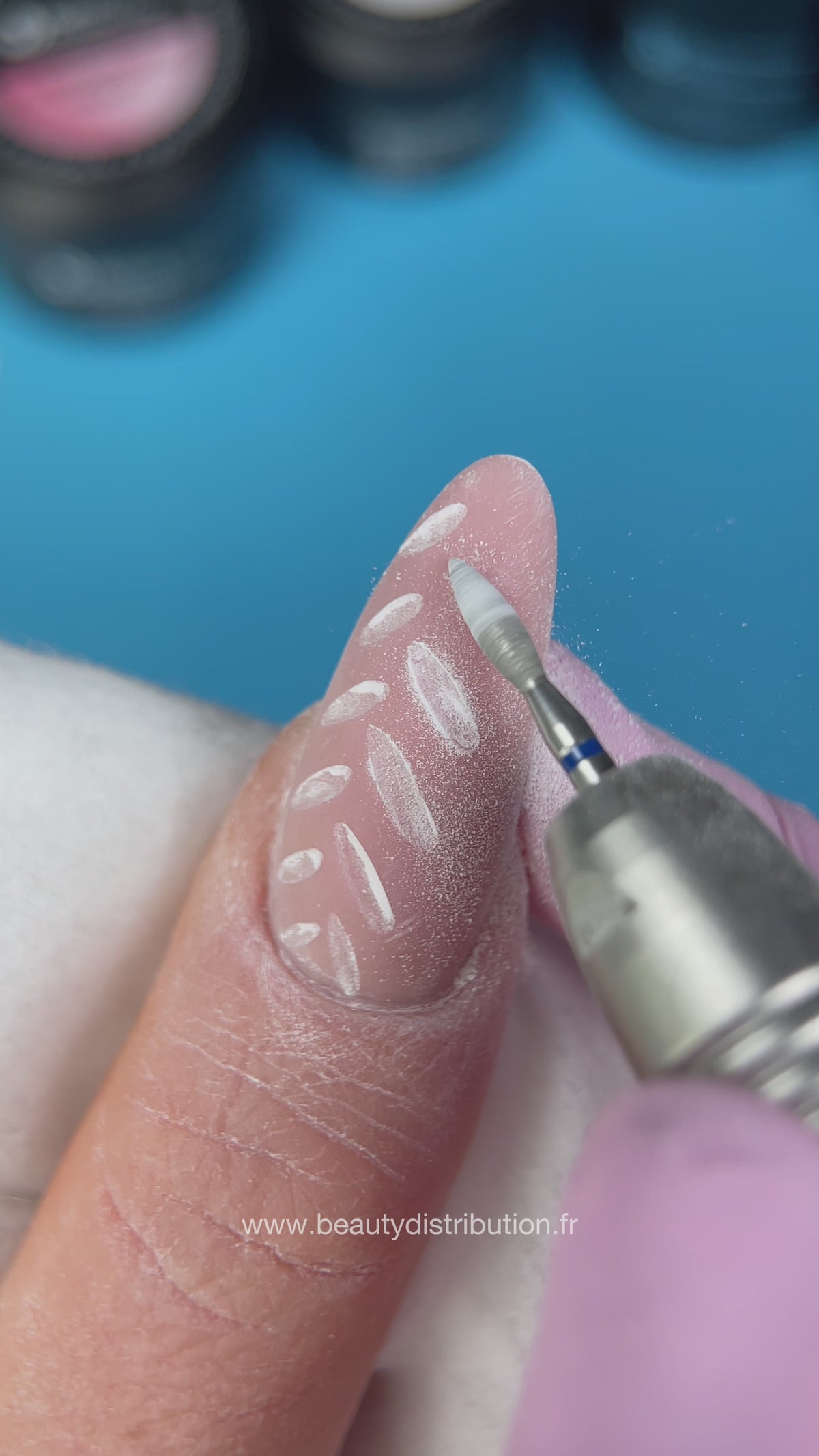 Travail à la ponceuse sur une manucure rose à motifs blancs
