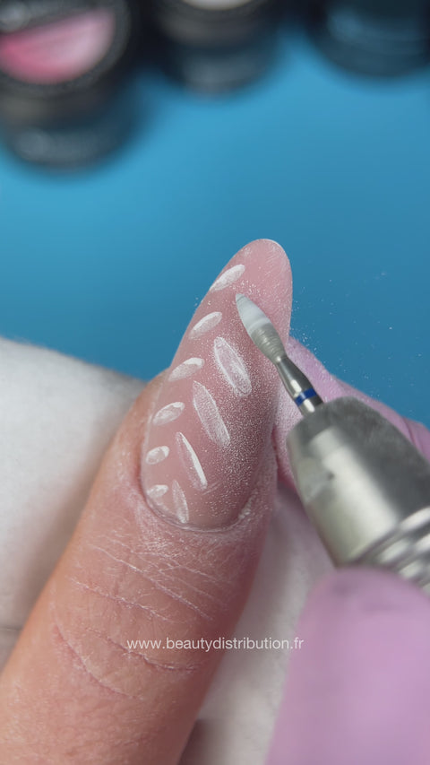 Travail à la ponceuse sur une manucure rose à motifs blancs